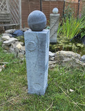 Decorative stone sphere on a pedestal in a garden setting with water and plants.